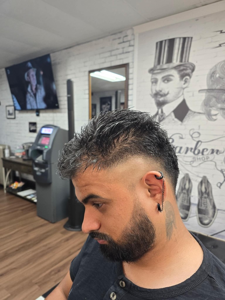 Side profile of client with high skin fade, styled top, and trimmed beard by the mural