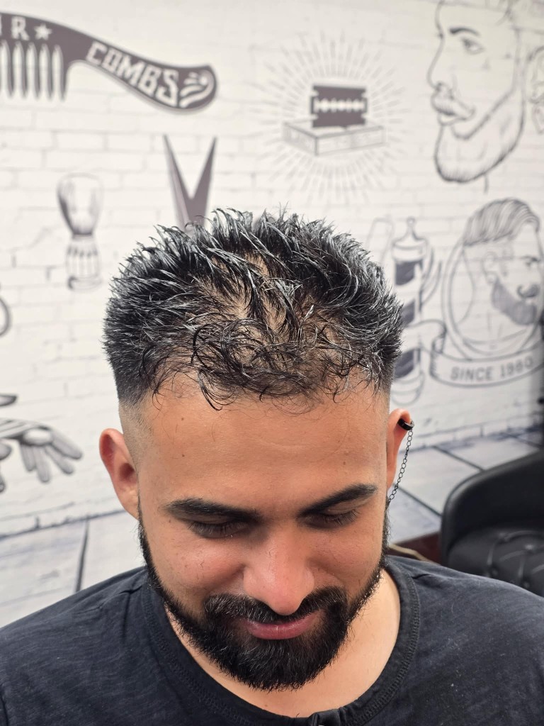 Client with textured crop, skin fade, and shaped beard in front of barber shop mural wall