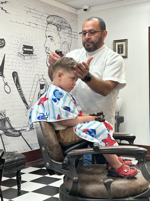 Willie cutting a young customer's hair, patriotic cape on, careful focus